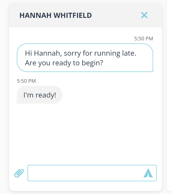 A chat window headed with the client name in capitals and a close cross. Below it a message from the provider in an outlined bubble on the right reading Hi Hannah, sorry for running late. Are you ready to begin? and the client reply in a filled bubble on the left reading I am ready, each with a time above it. At the foot is a paper clip button and an empty text box with a send arrow.